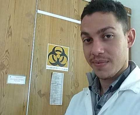Estudante do sexo masculino de jaleco em frente à porta do laboratório