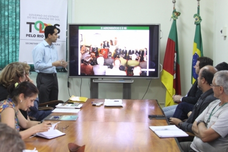 grupo de pessoas em volta de uma mesa assistindo a uma apresentação em power point